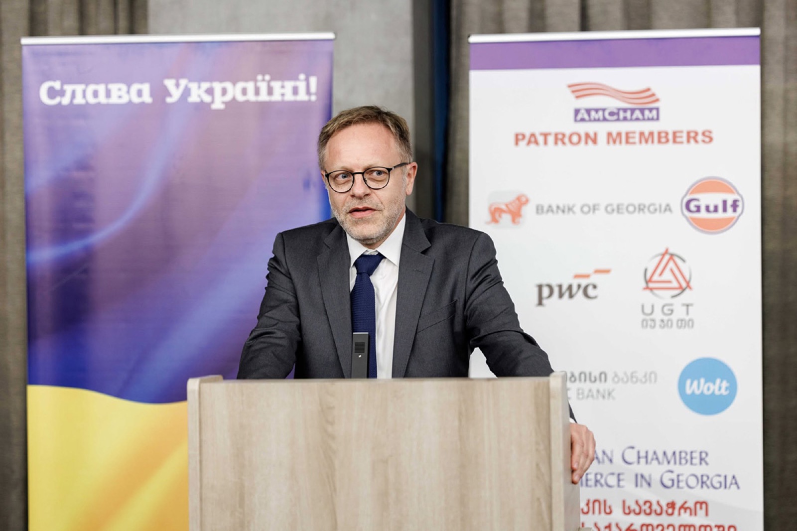 A speaker at a lectern beside a patron members banner
